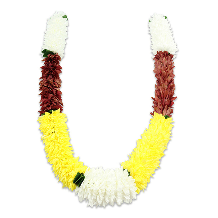 A traditional, U-shaped floral mala is presented here with attention to every petal and seam, foregrounded against a pure white studio background that highlights its colour segmentation and textural richness. At each top end a dense, cylindrical segment of creamy white, small, tightly packed petals forms a soft, cushion-like beginning-these mimic tiny chrysanthemums or jasmine clusters, lending an airy, ceremonial grace. That white section transitions into a substantial maroon or deep reddish-brown band, composed of equally close-set synthetic flowers that add weight and a grounded warmth to the upper curve. The longest, most visually dominant portion of each arm is a bright yellow sweep crafted from numerous plush, marigold-reminiscent petals; this sunny stretch gives the garland its generous arc and festive character. Where the two yellow arcs meet at the bottom, a larger, lush cluster of pure white chrysanthemum-like blooms creates the focal centre, subtly punctuated by small dark green leaf accents which serve as elegant dividers between the colour blocks. The construction is meticulous: thousands of fabric petals layered and stitched to emulate the fullness of live blooms, with a matte textile finish and the faint scent of fabric rather than botanical perfume. Gentle lighting produces a soft shadow beneath, offering depth and the suggestion of weight if the garland were to be lifted. This piece is suited to Hindu pooja settings, wedding ceremonies, temple offerings or home festival décor; pictured in my mind it would look at home on Esher High Street during celebrations, adorning community altars at local halls, or greeting guests near Claremont Fan Court with its colours symbolising purity, prosperity and devotion.